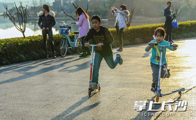 今日上午，明媚的阳光时而穿过云层，梅溪湖畔，两位小朋友穿着单衣正开心的玩耍着滑板车。长沙晚报记者 邹麟 摄
