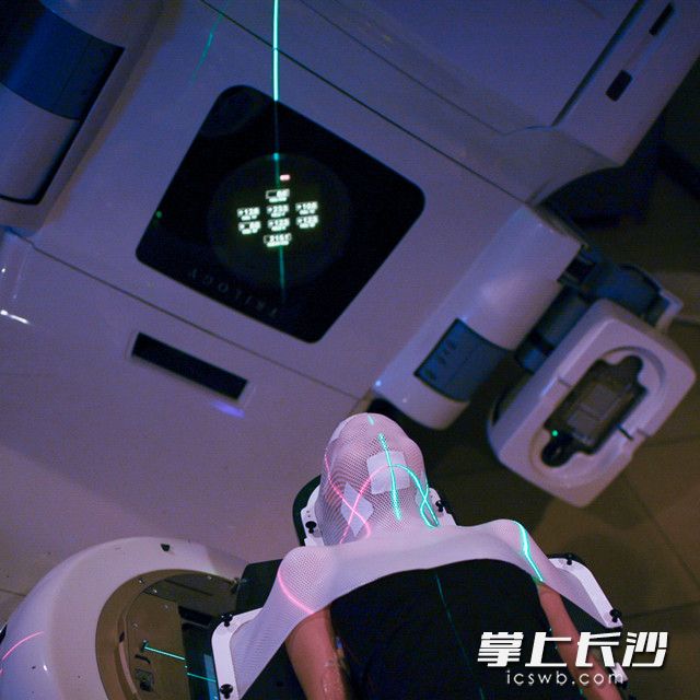 治疗室内，一位患者躺在治疗床上，三维激光灯投射于患者面罩的上并与标记重叠，达到精确定位的目的。