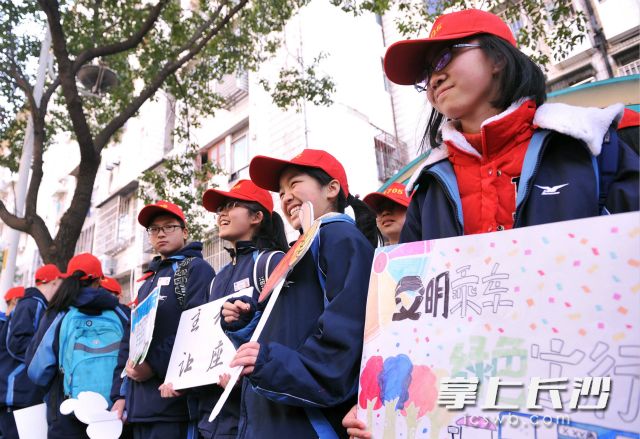 学生志愿者手持自绘的宣传牌，在劳动广场公交调度室附近倡导市民文明出行。