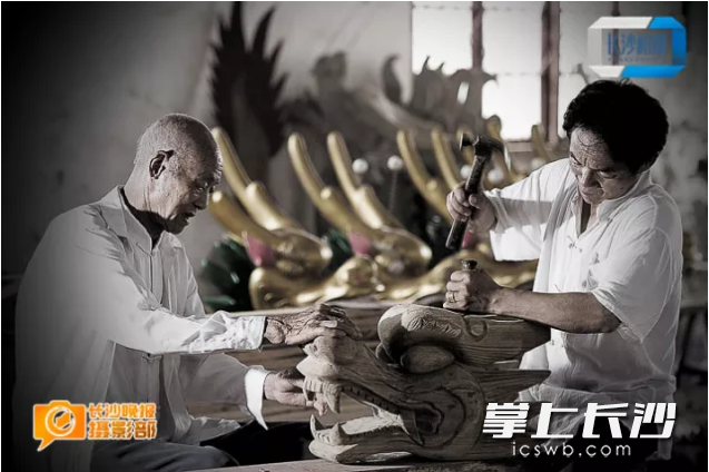 2012年6月17日，民间龙舟打造技艺传人许桂生和徒弟在作坊中雕琢“龙头”。
