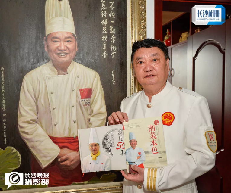 　　2018年9月20日，在王墨泉家里，国宝级湘菜大师王墨泉拿着自己从业50年的画册和菜谱在油画像前合影。