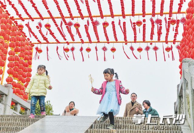 靖港古镇石拱桥上挂满了灯笼，两位小朋友拿着糖画开心地玩耍。