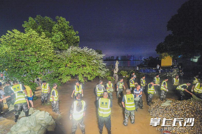 7月1日晚11时，湘江风光带万达广场段，开福区城管工作人员正在抓紧传递沙袋修筑子堤。 长沙晚报记者 邹麟 李锋 摄