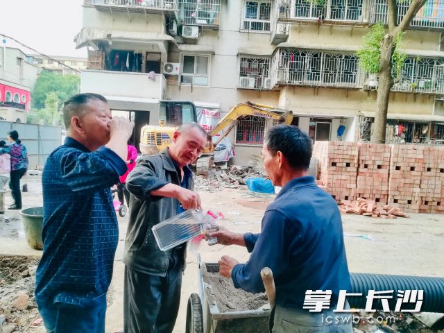 热心居民骆建峰（中）给工人端茶送水，支持拆违整治。 通讯员 曹露 摄