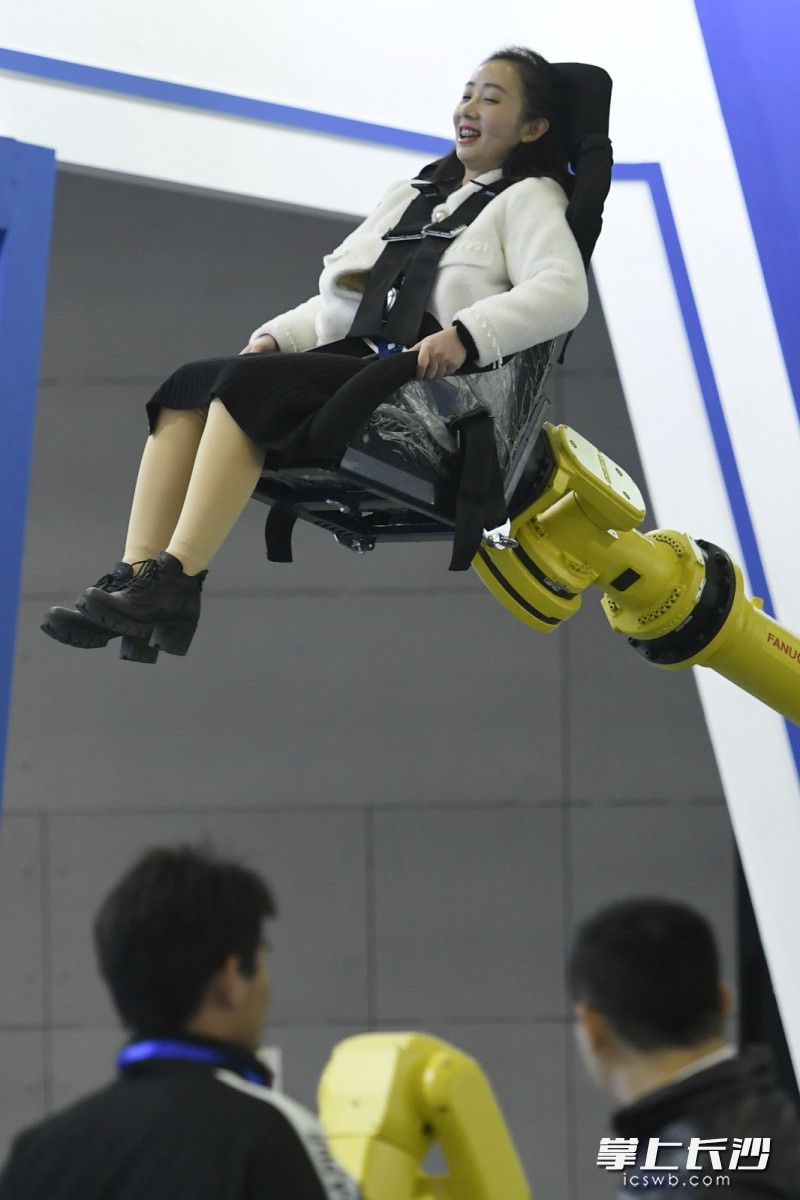 在机器人展台，一个观众正在体验机械臂蹦极，表情颇为夸张。