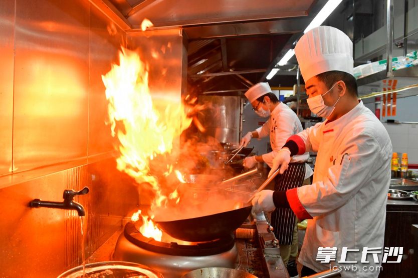 玉楼东湘府路旗舰店后厨内，戴着口罩、一次性手套的厨师在精心烹饪各种美食。