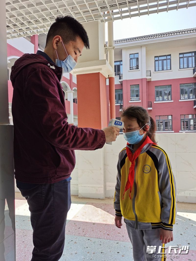 为保障学生在校健康，清水塘江湾小学采取了多项防疫措施。图为老师给学生测量体温。