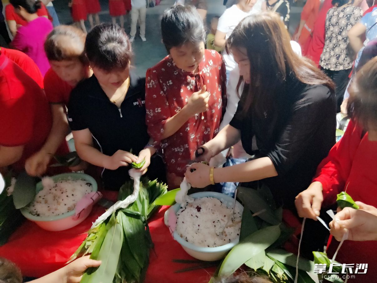 社区年轻的党员向巧手的志愿者阿姨耐心请教包粽子的技巧，传承传统文化。