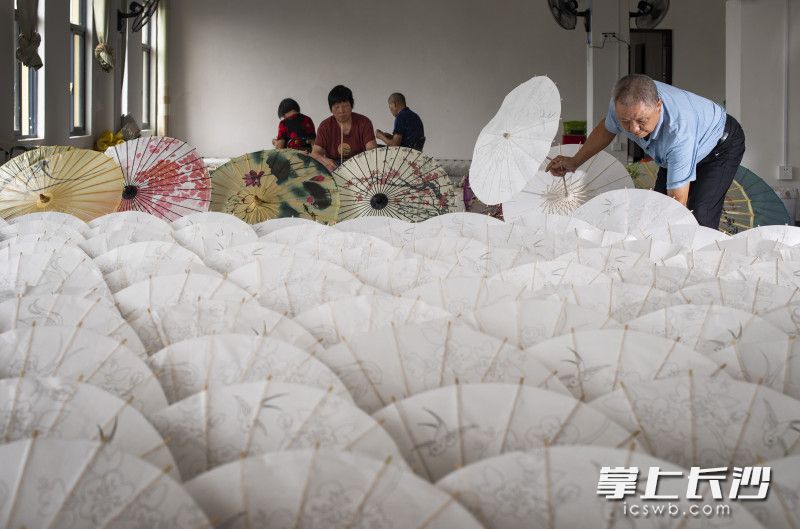 村民们在浏阳市达浒镇椒花新村的的“致富工厂”里集中工作，通过制作工艺油纸伞，每人每天能挣到120元左右。
