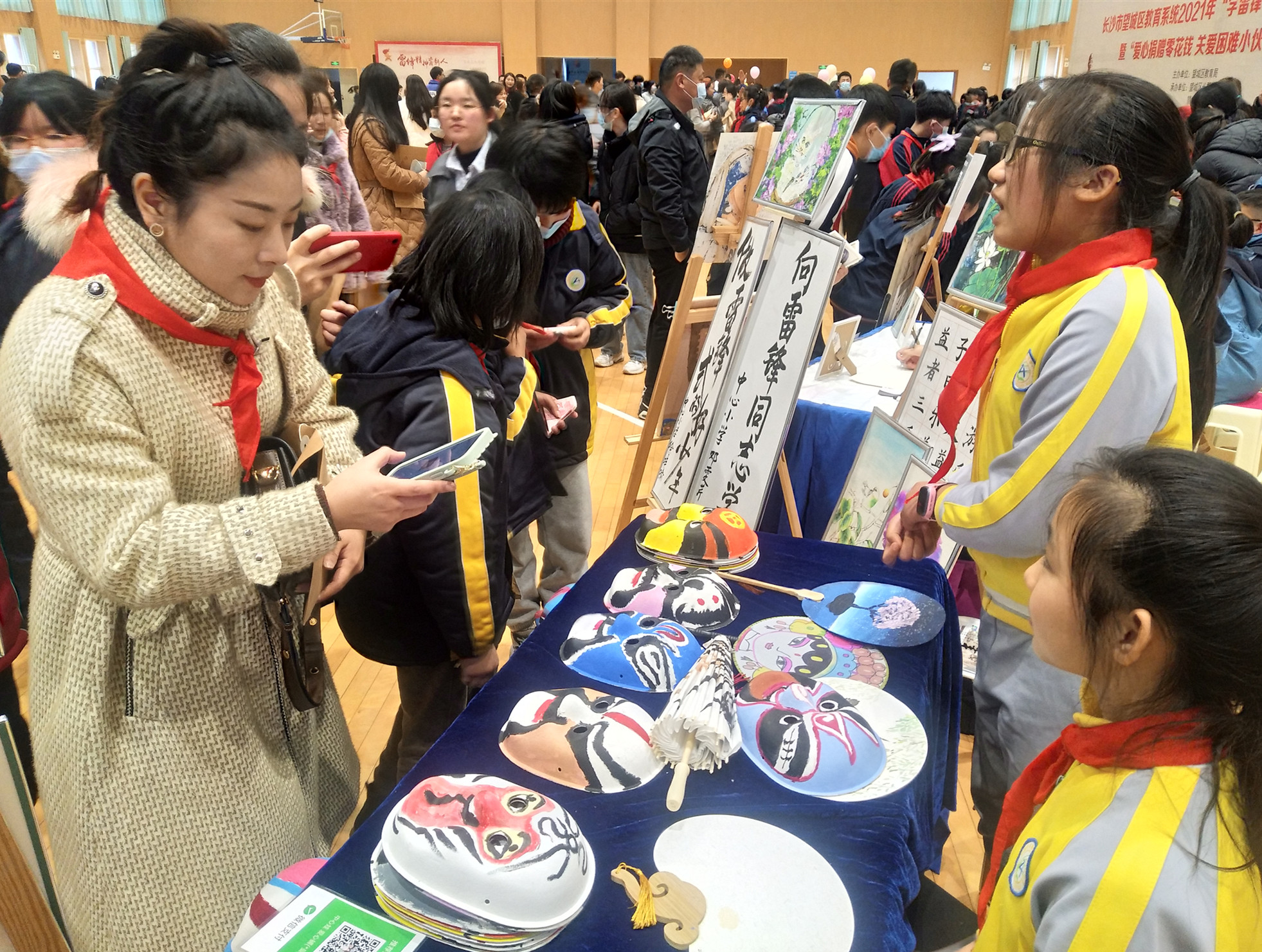 一位嘉宾正在购买孩子们手工制作的京剧脸谱面具。