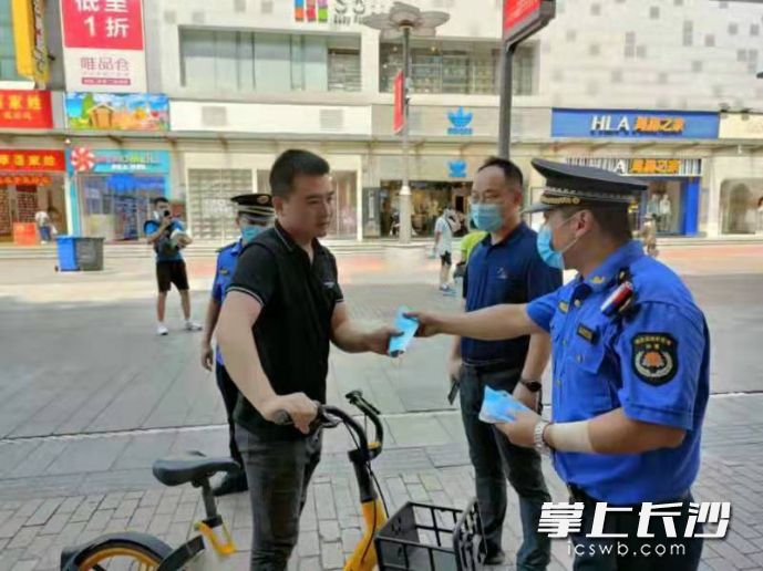 在黄兴南路步行商业街，城管执法队员为市民游客送上口罩并进行防疫宣传和提示。