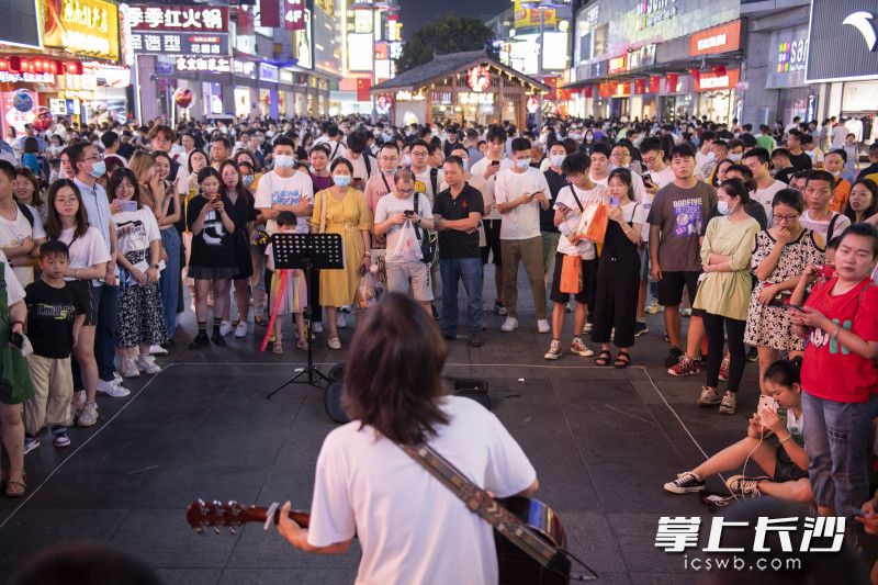 在黄兴南路步行街，游客们在欣赏街头歌手的表演。