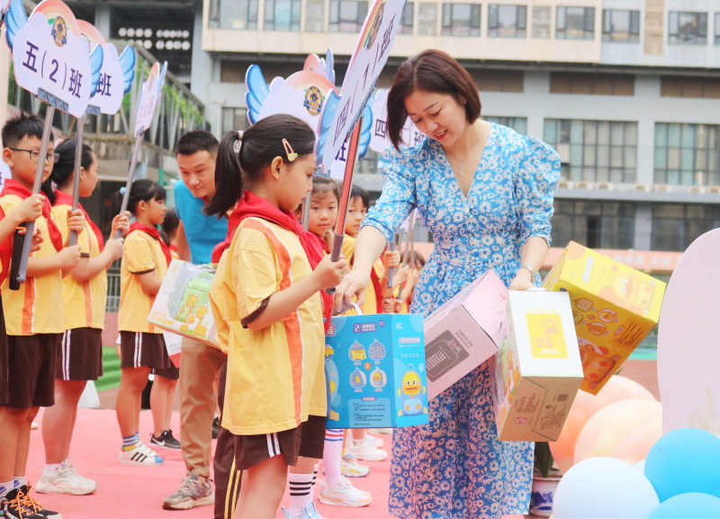 怡海小学校长王敏（右一）给同学们赠送爱心存钱罐。