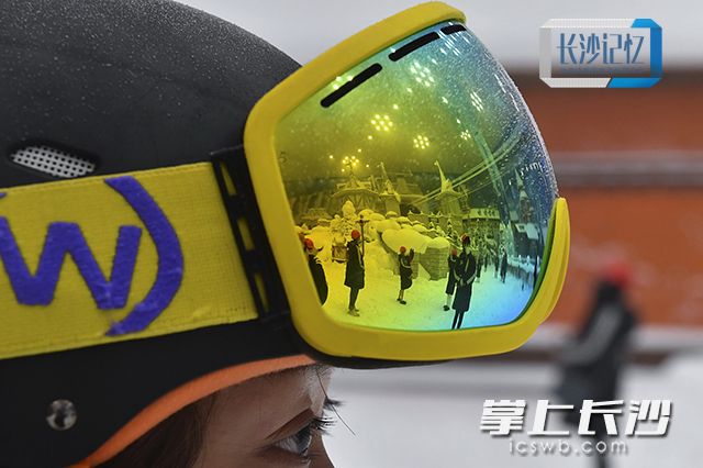 一名滑雪教练的护目镜里，倒映着欢乐雪域的北欧风格小镇和参观的游客。
