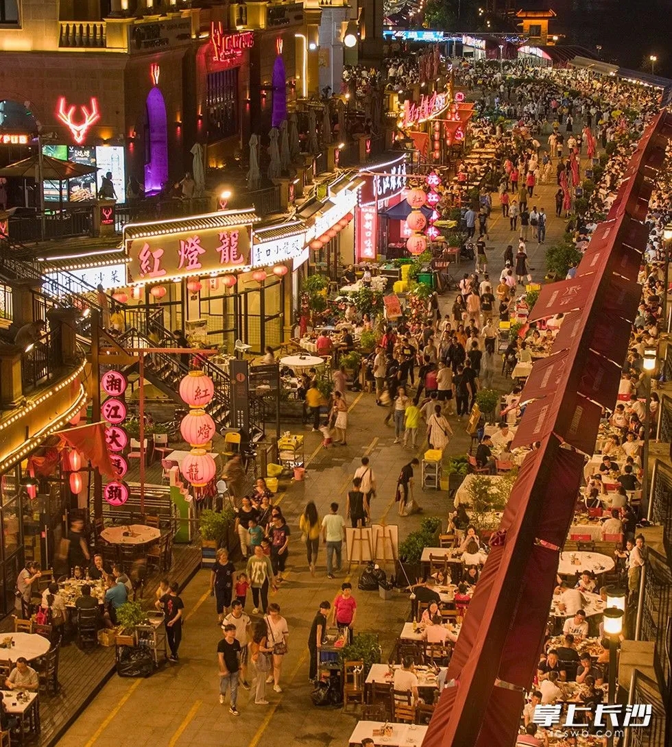 潇湘北路的渔人码头美食街，有序摆放的露天餐桌、摊担前，吃夜宵或排队的人群与前来纳凉的的路人交织。
