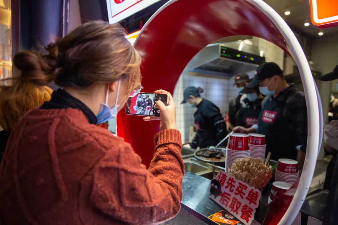 长沙网红店“黑色经典”内，一名游客一边排队一边用手机拍摄美食制作过程。